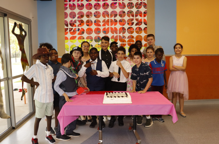 A group of people standing around a table with a cake on it