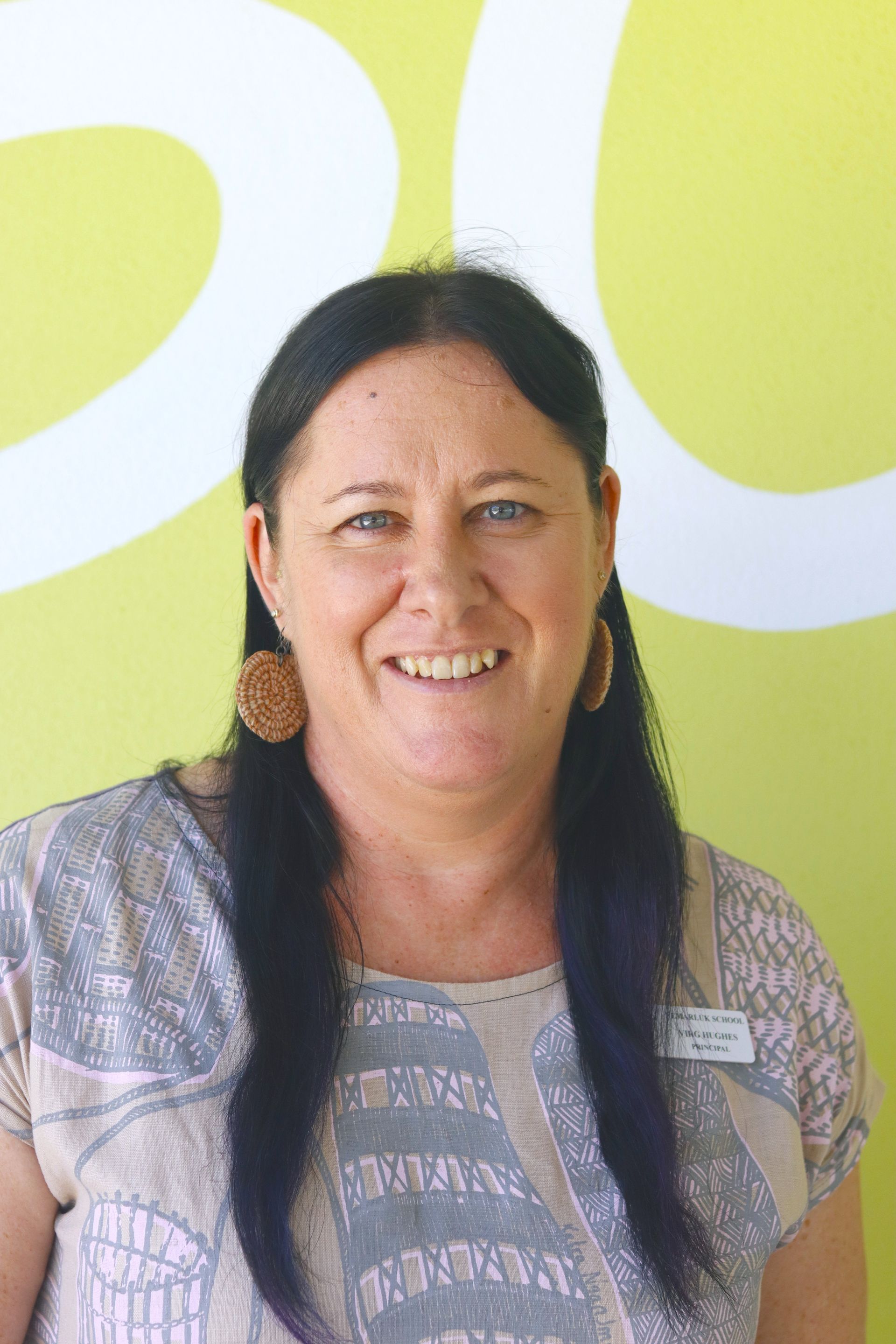 A woman with long black hair is smiling in front of a yellow wall.