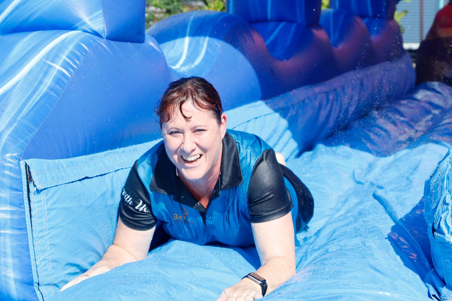 A woman is laying on a blue inflatable slide and smiling.