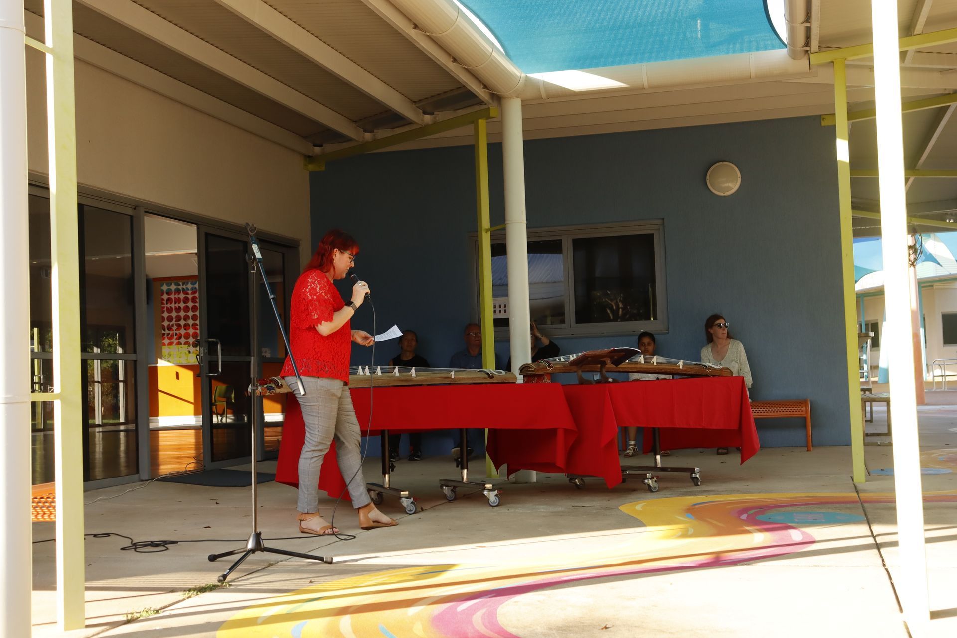 A woman in a red shirt is standing in front of a microphone