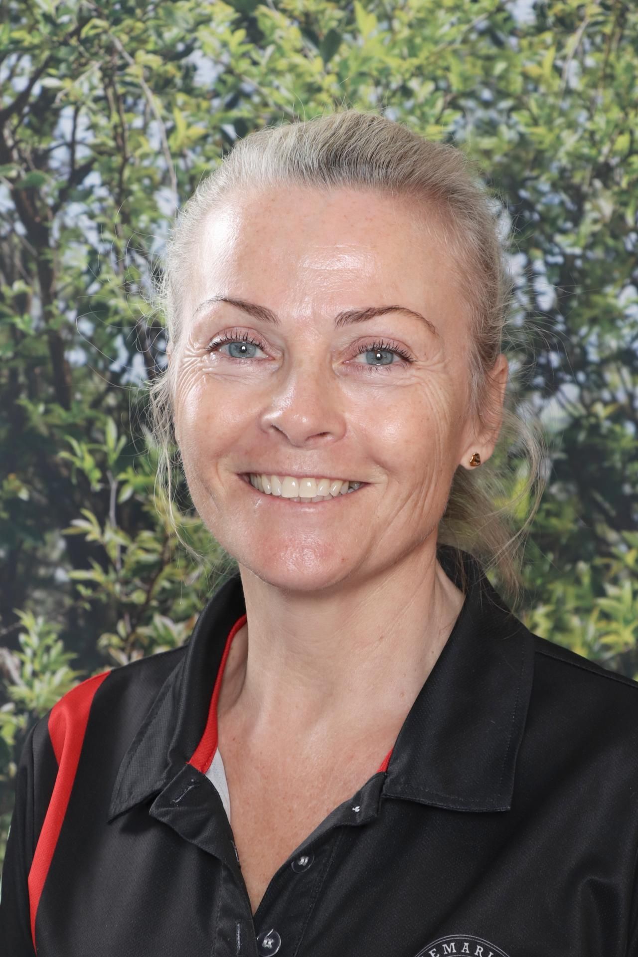 A woman in a black shirt is smiling in front of a blue background.