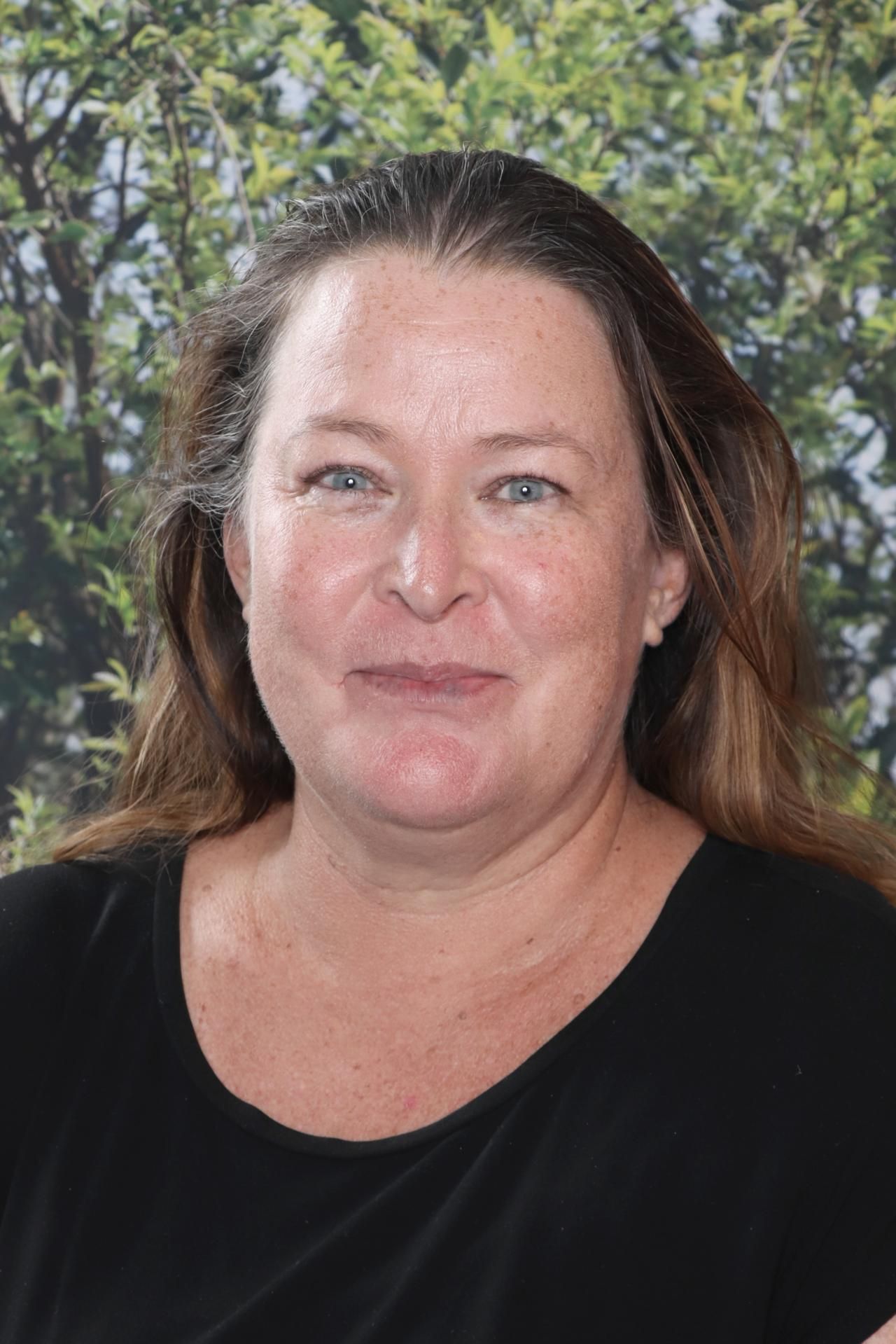 A woman wearing glasses and an orange shirt is smiling for a picture.