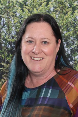 A woman with long black hair is smiling in front of a yellow wall.