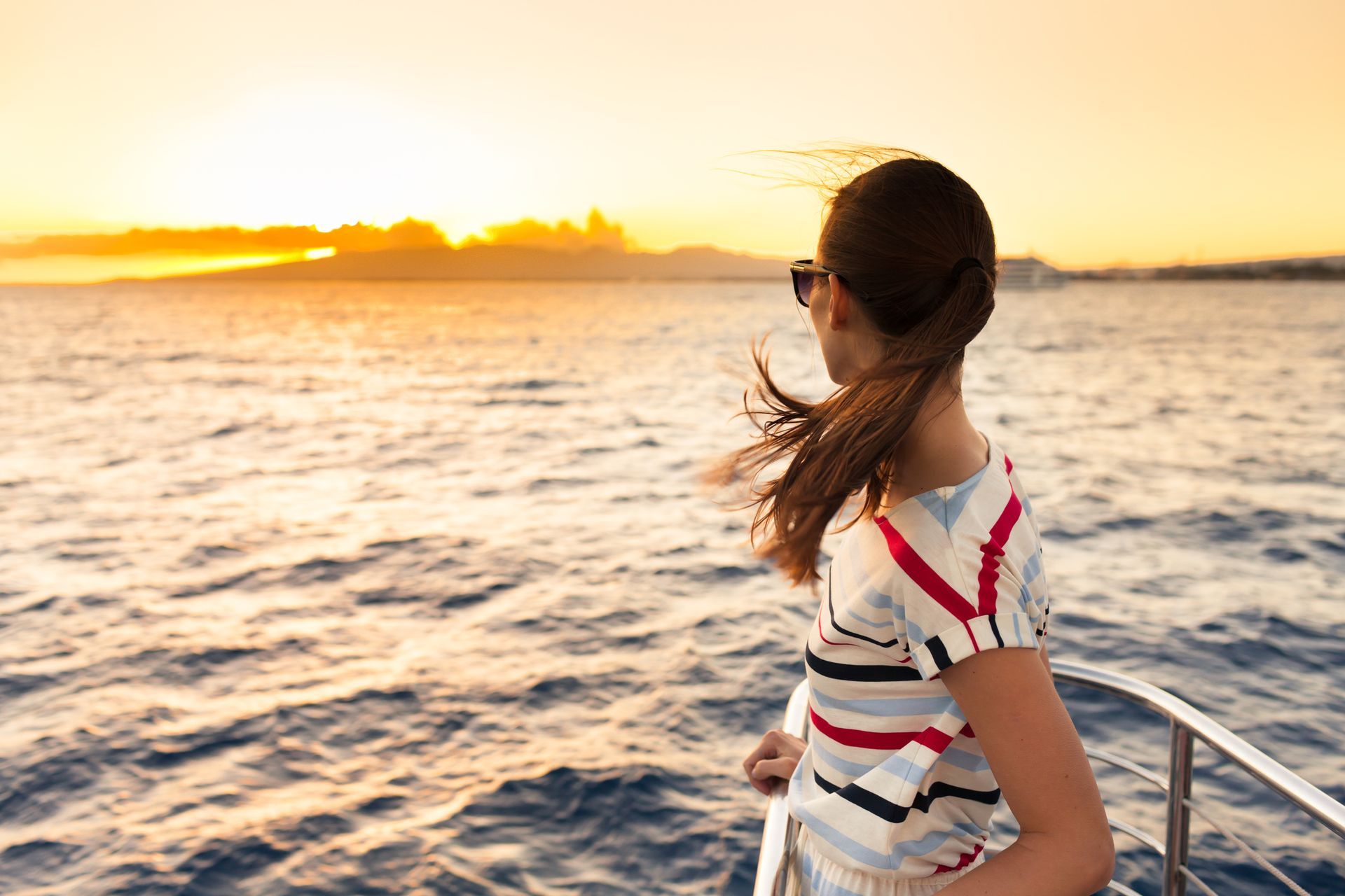A woman is standing on a boat in the ocean at sunset.