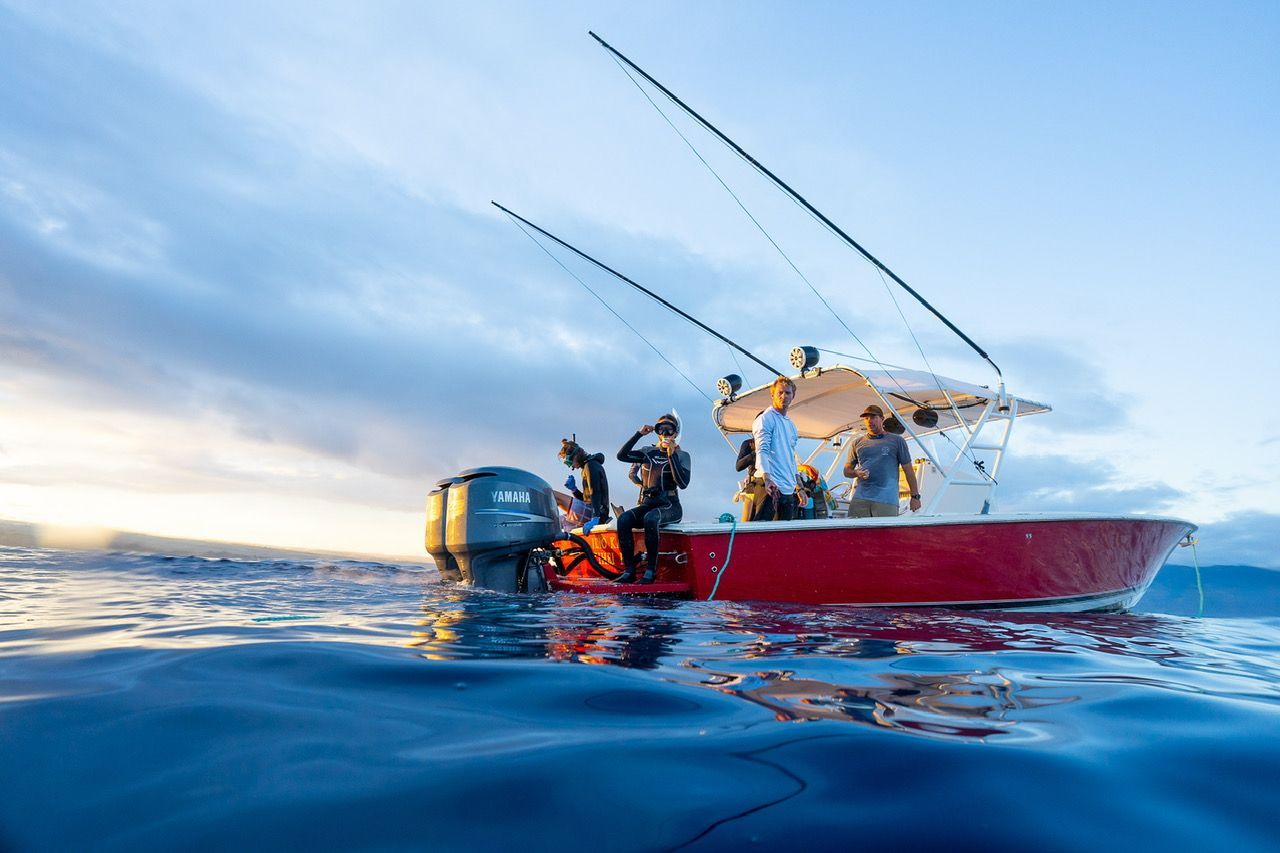 A red fishing boat with people fishing on a sunny day.