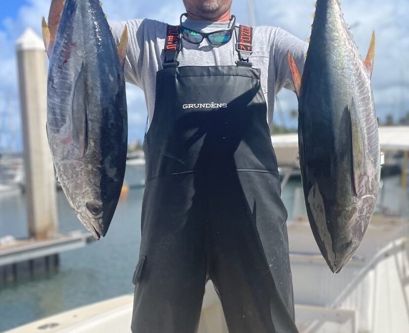 A man in overalls is holding two fish in his hands