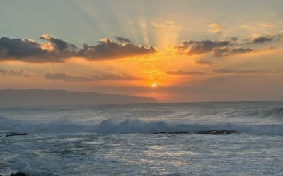 The sun is setting over the ocean with waves crashing on the shore.