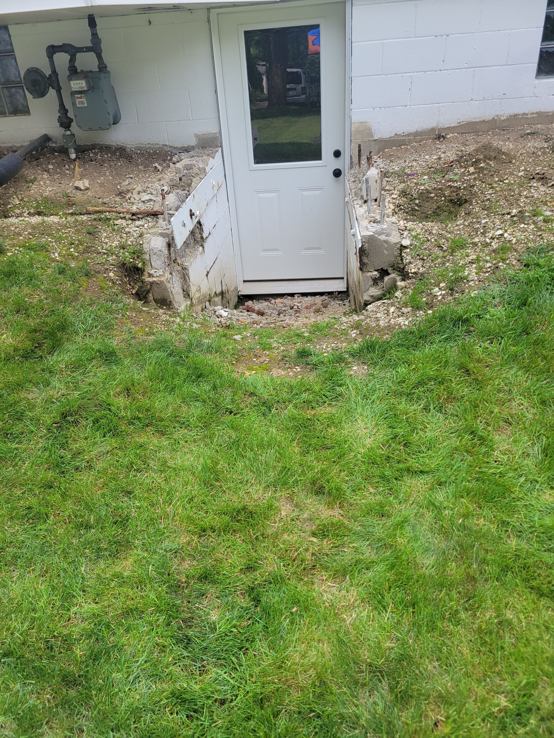 White door recessed into a foundation wall; overgrown grass in front, sloped dirt on either side.