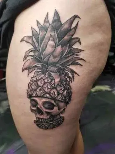 Black and gray pineapple skull tattoo on a person's thigh.