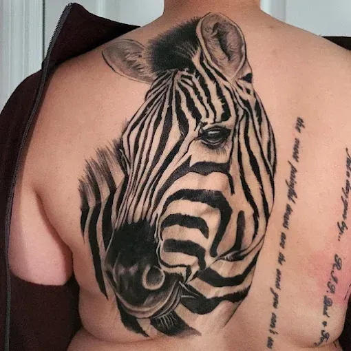 Black and white zebra head tattoo on a person's back, with text on the right side.