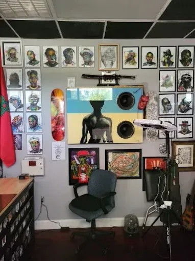 Tattoo studio interior with artwork-covered walls, speakers, a skateboard, and a tattoo chair.