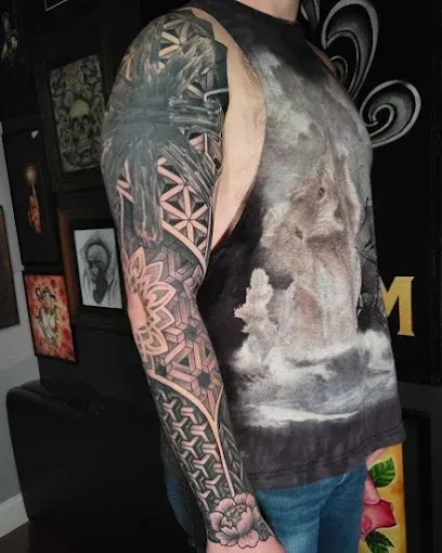 Person with full-sleeve geometric tattoo, floral hand tattoo, wearing graphic t-shirt and jeans, indoor setting.