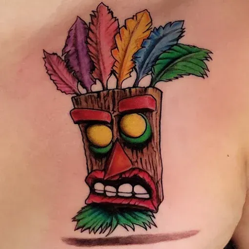 Tattoo of Aku Aku mask, from Crash Bandicoot, with colorful feathers, and angry expression.