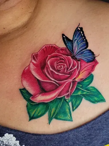 Rose tattoo with a blue butterfly on the chest, detailed red rose, green leaves, and blue butterfly.