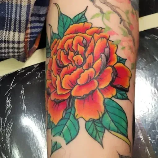 Bright orange peony tattoo with green leaves on arm.