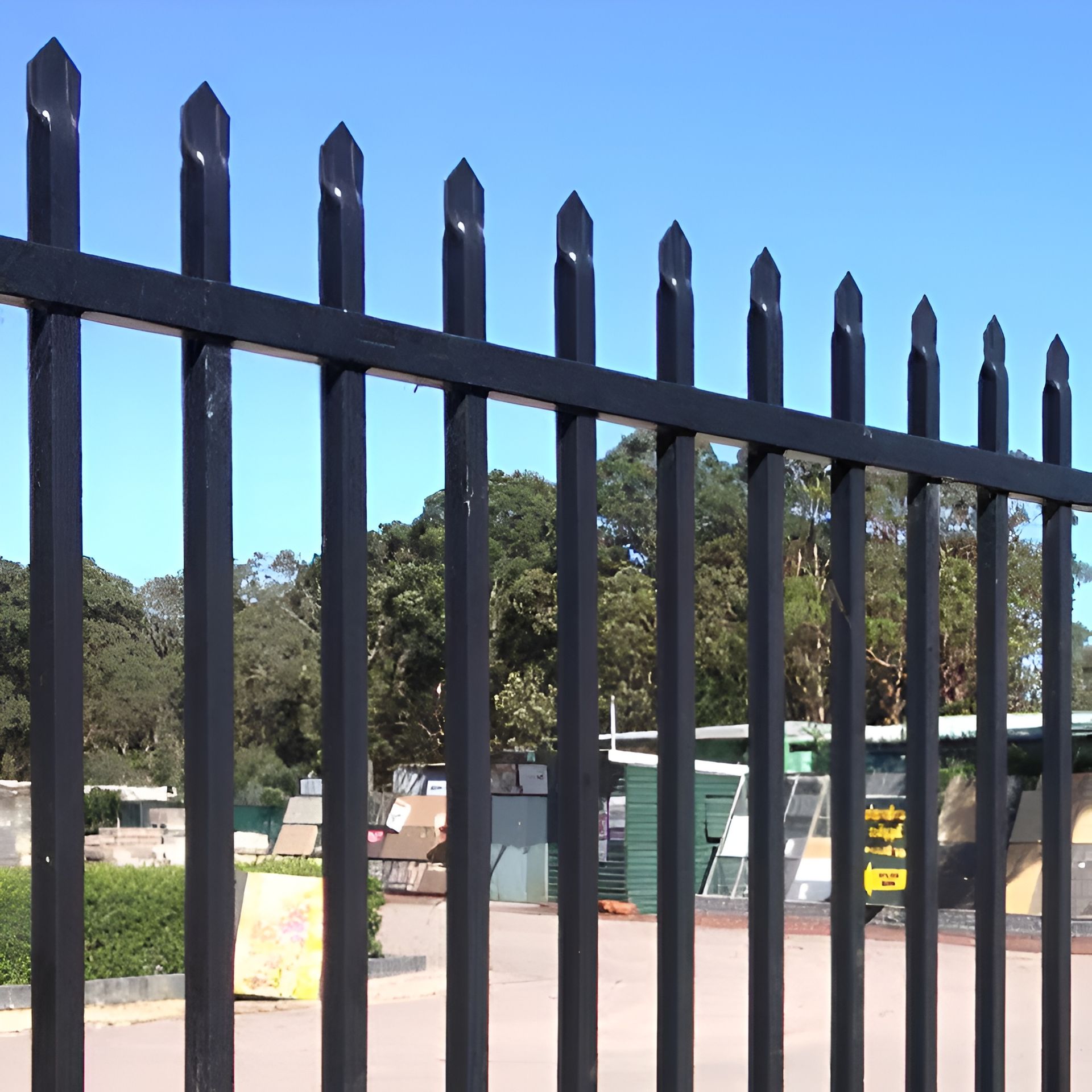 Black Metal Fence With Pointed Tops, Green Trees in Background, Blue Sky — Metal Fencing Supplies In Harrington, NSW