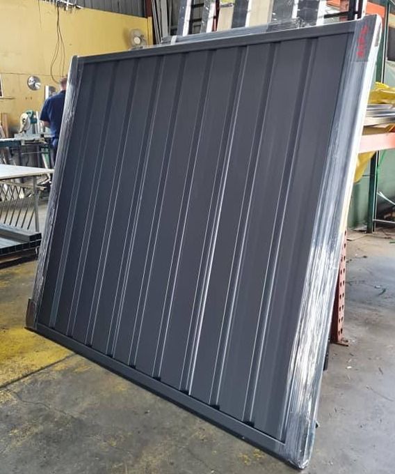 Gray Metal Fence Panel, Vertical Ribbed Design, Wrapped in Plastic, in a Workshop — Metal Fencing Supplies In Taree, NSW