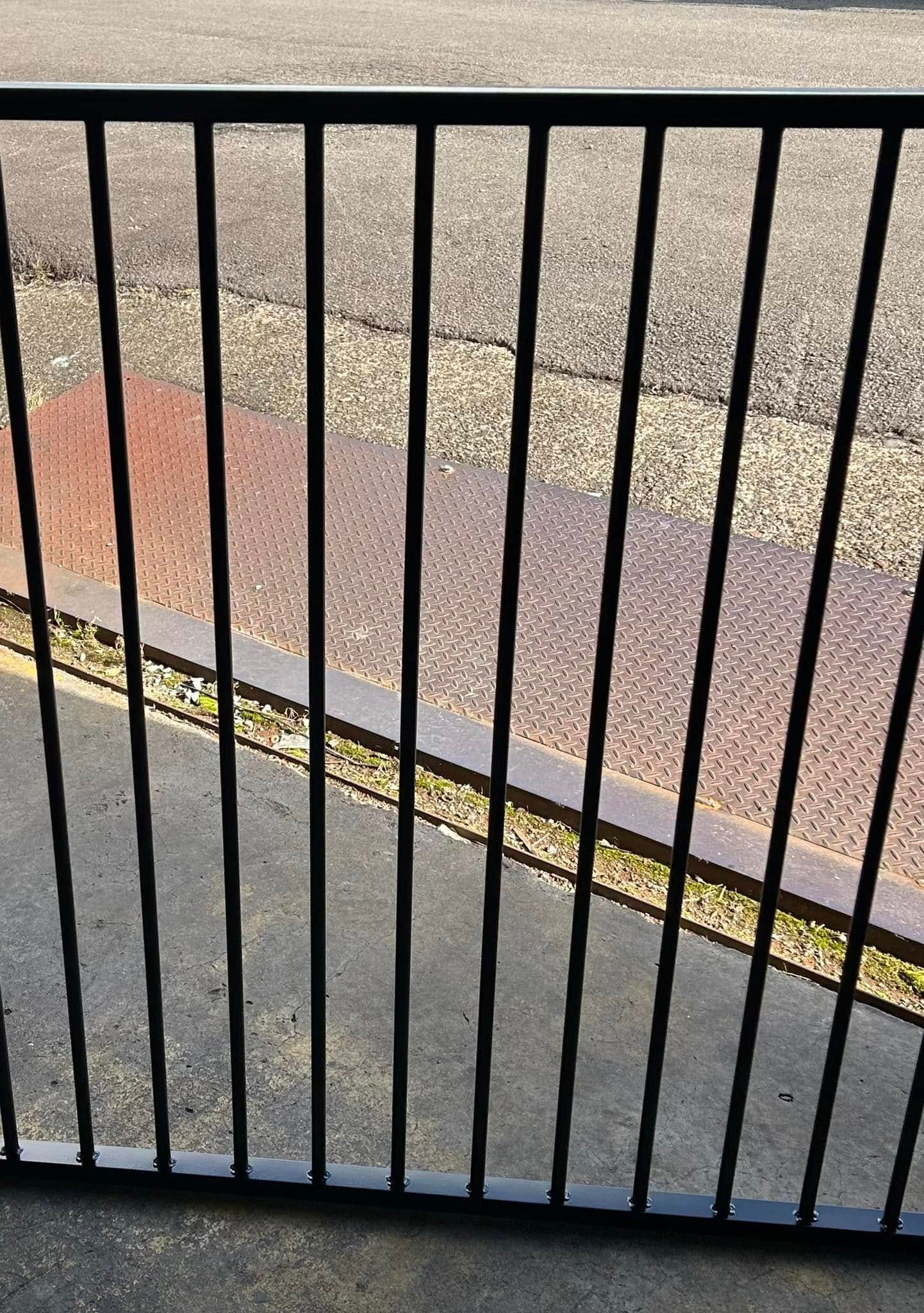 Black Metal Fence With Vertical Bars Casting Shadows on Concrete and Brick — Metal Fencing Supplies In Taree, NSW