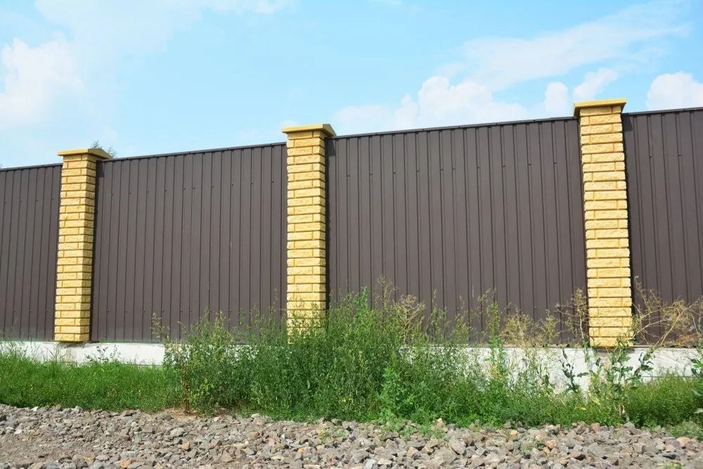 Brown Metal Fence With Yellow Brick Pillars, Green Grass, and Blue Sky — Metal Fencing Supplies In Taree, NSW
