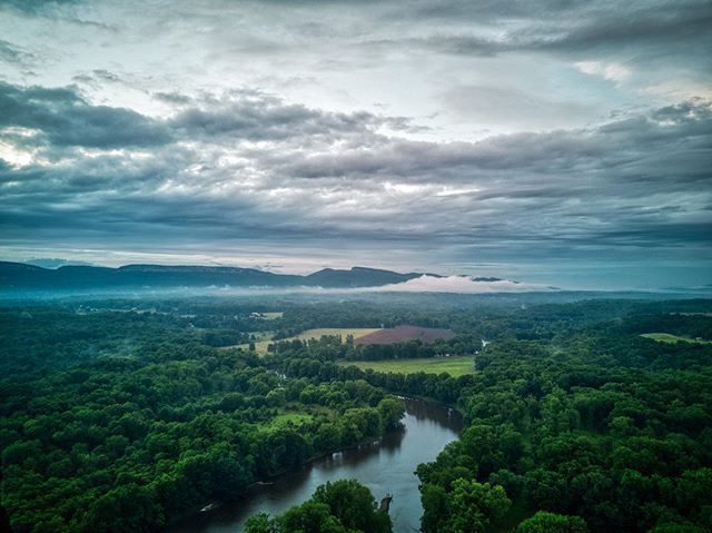 Aerial view of a tranquil river surrounded by trees by Hudson Valley Drones on a cloudy day.