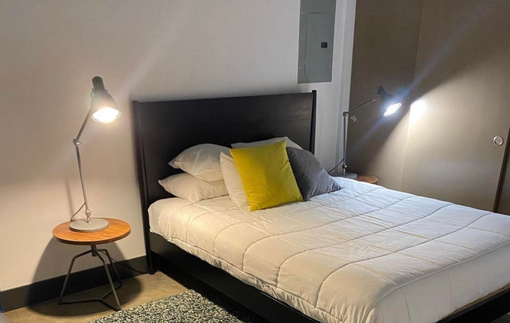 A modern bedroom featuring a bed with white bedding, yellow and gray pillows, and two side lamps on small round tables.