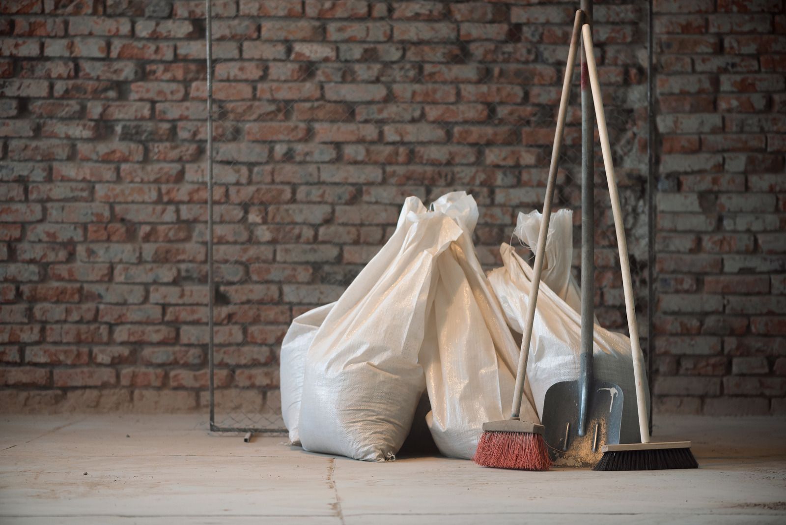 Trash bags and cleaning tools leaned against a brick wall in a garage or storage area.