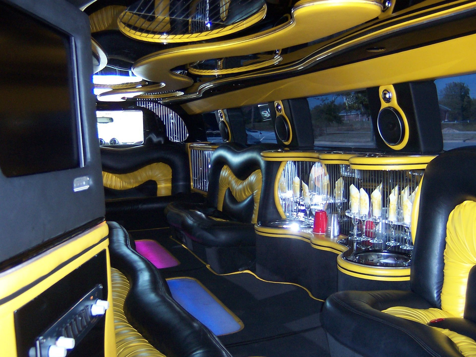 Luxurious black-and-yellow limousine interior with leather seating, bar area, and neon ceiling lights