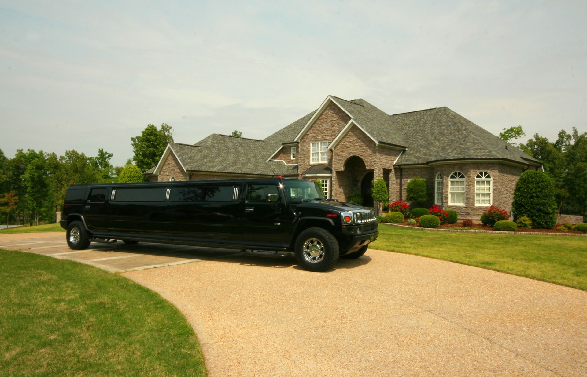 Black limousine parked on a curved driveway in front of a large brick house.
