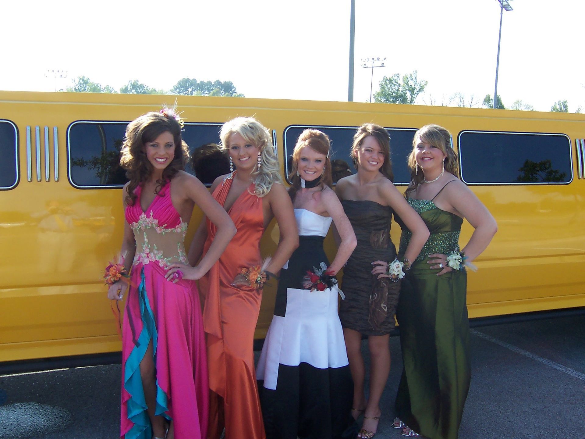 Five people posing in colorful outfits in front of a yellow limousine.