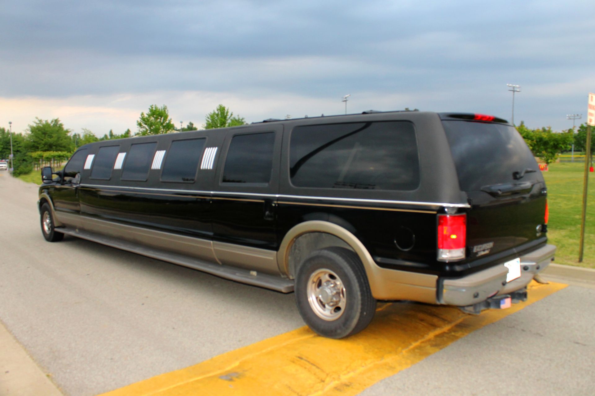 Black stretch limousine parked on a road with yellow lane markings under a cloudy sky