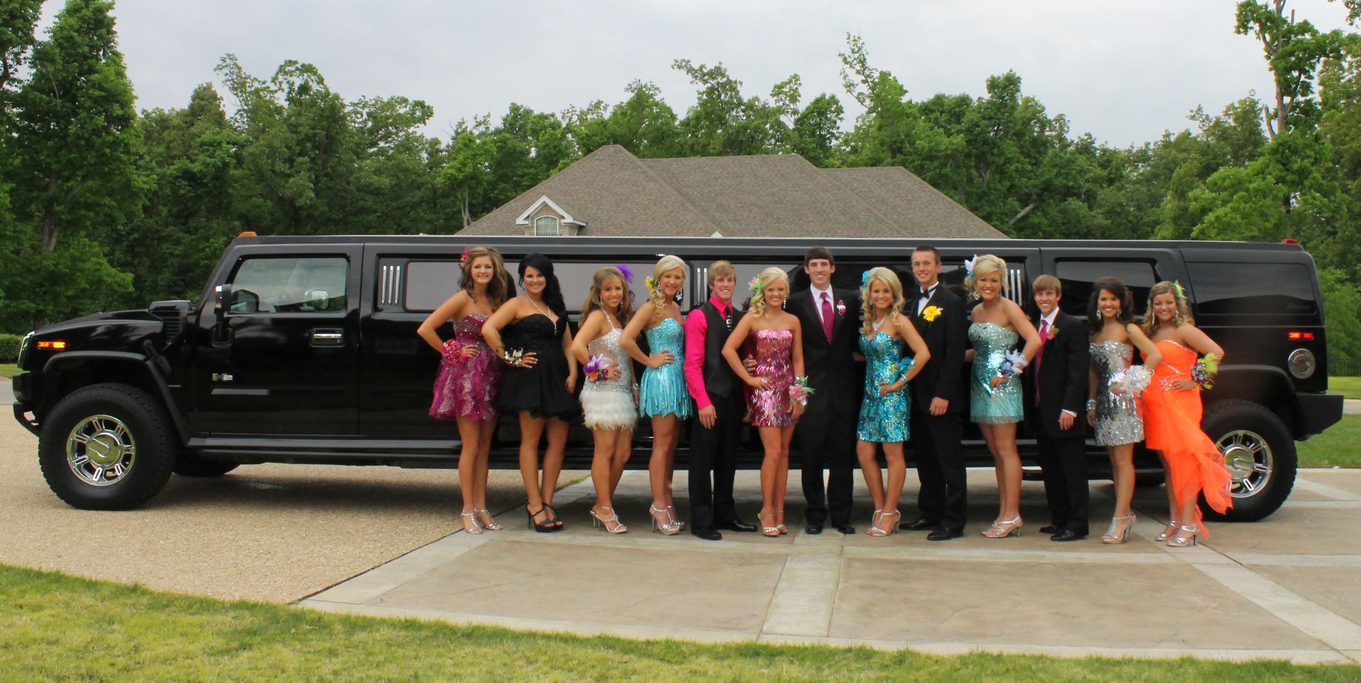 Group posing beside a long black limousine in a driveway, with a house and trees in the background