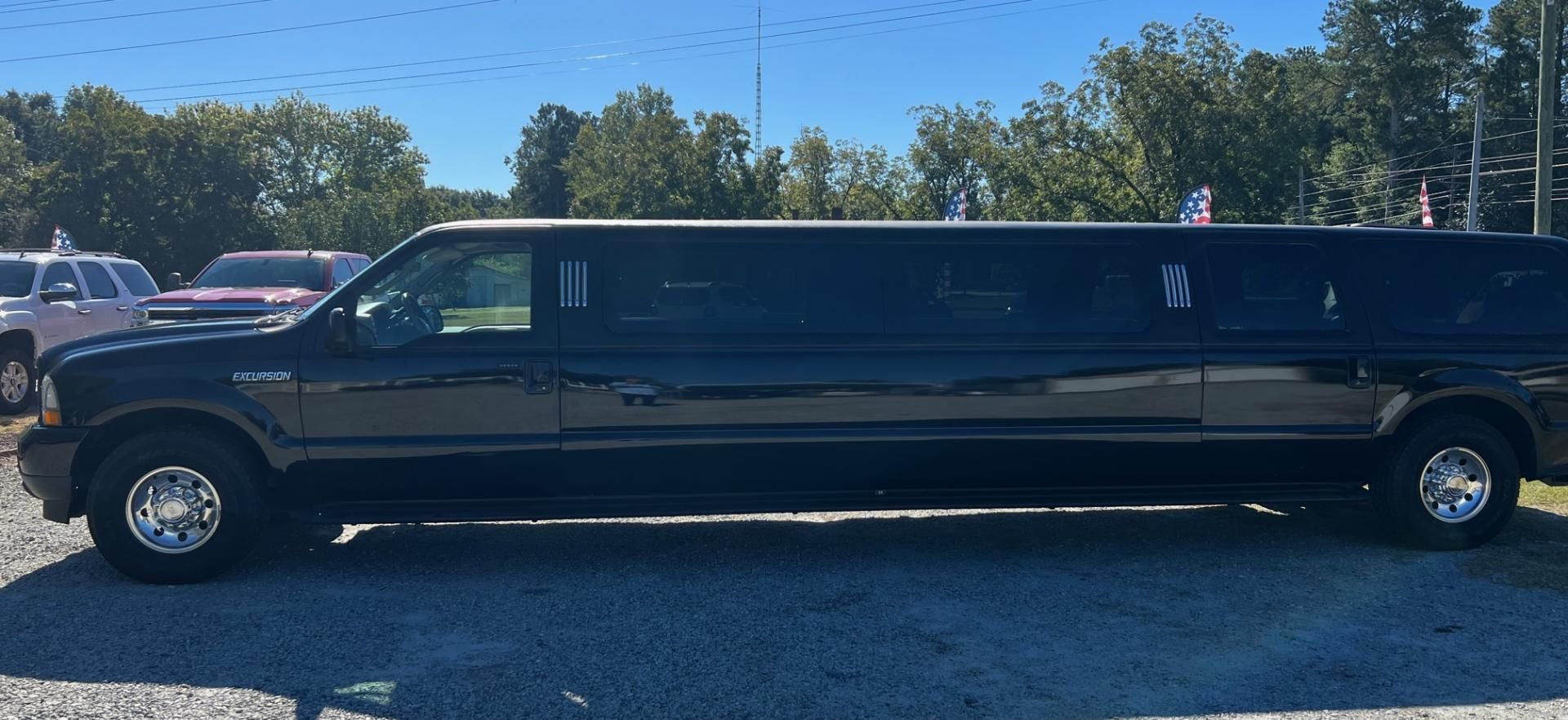 Black stretch limousine parked on a gravel lot under a clear blue sky