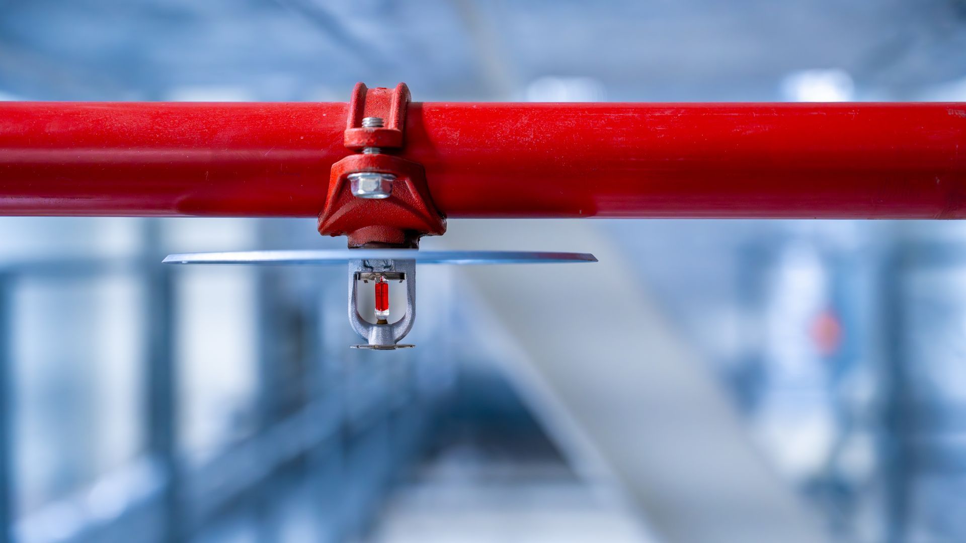 Close-up of fire sprinkler head mounted on red pipe in an industrial building ceiling.