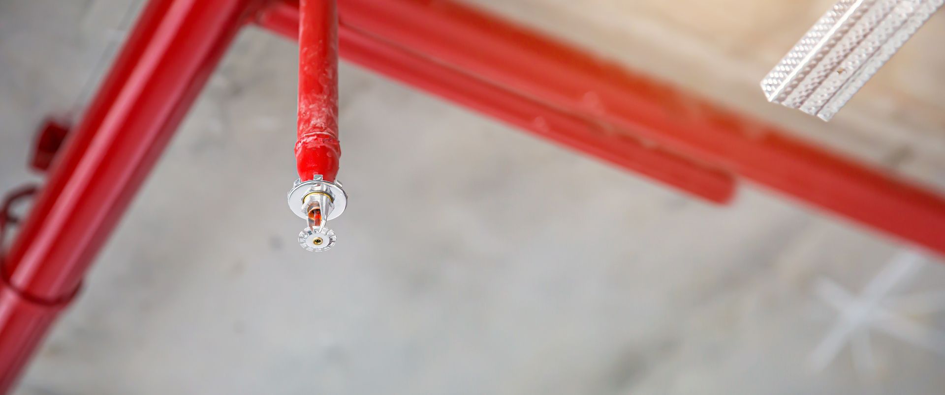 Red fire sprinkler pipe with a sprinkler head mounted on a ceiling in a building interior Red fire sprinkler pipe with a sprinkler head mounted on a ceiling in a building interior