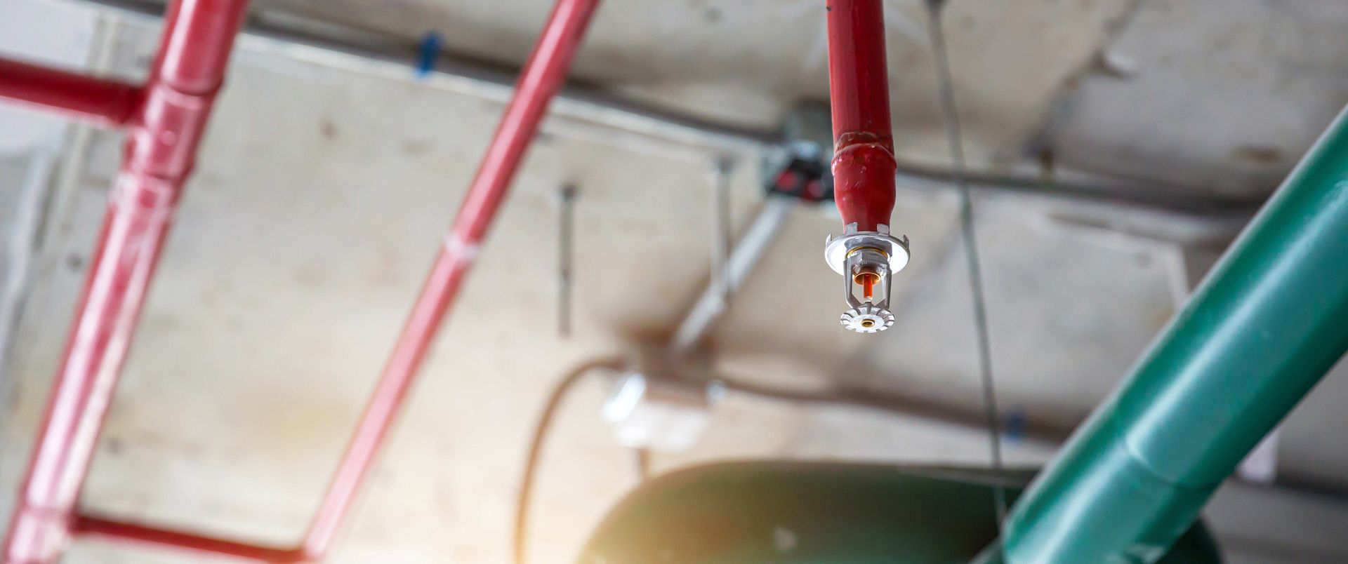 Ceiling-mounted fire alarm sprinkler system with red piping in an industrial building.