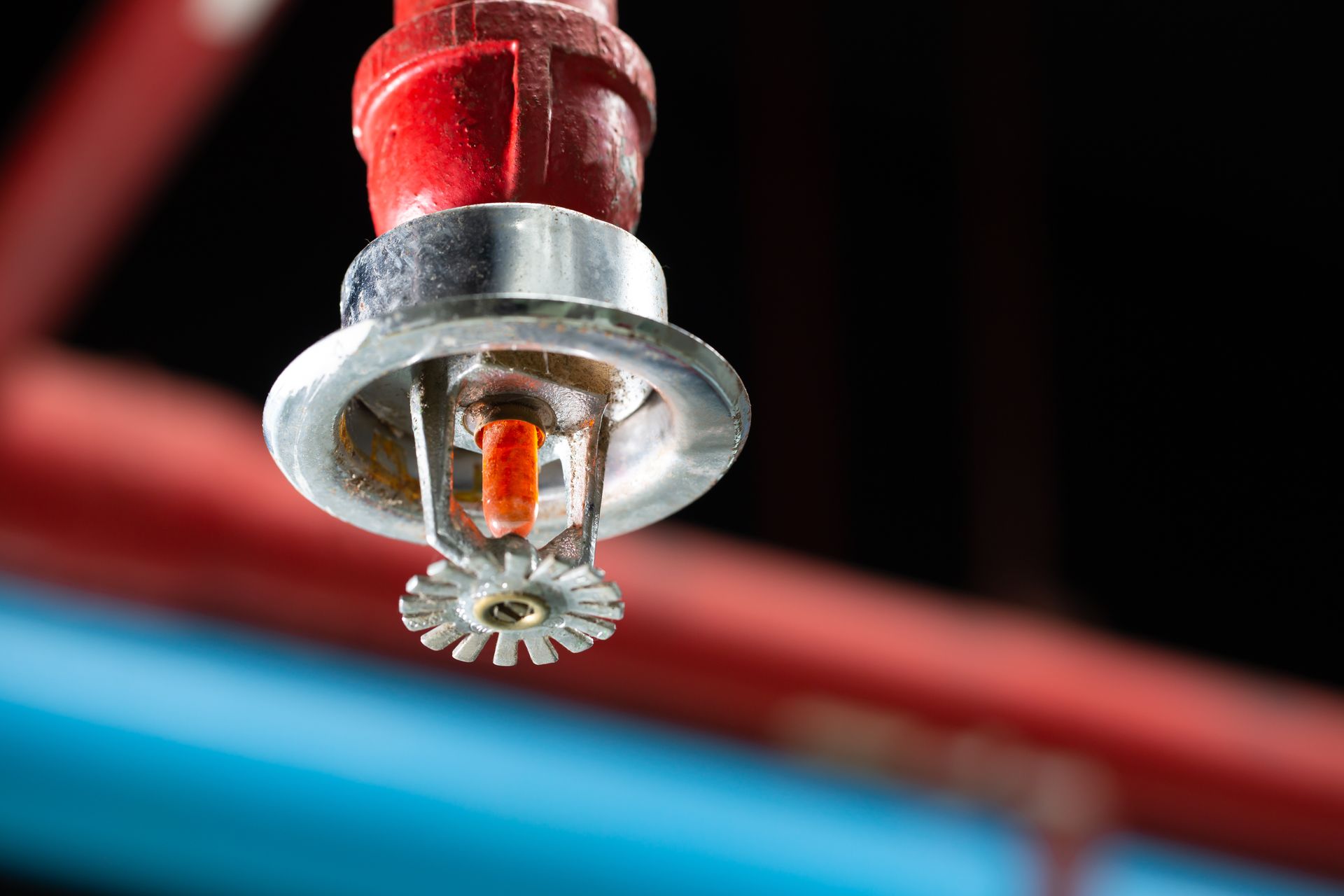 A fire sprinkler head on a red ceiling pipe inside a building interior area
