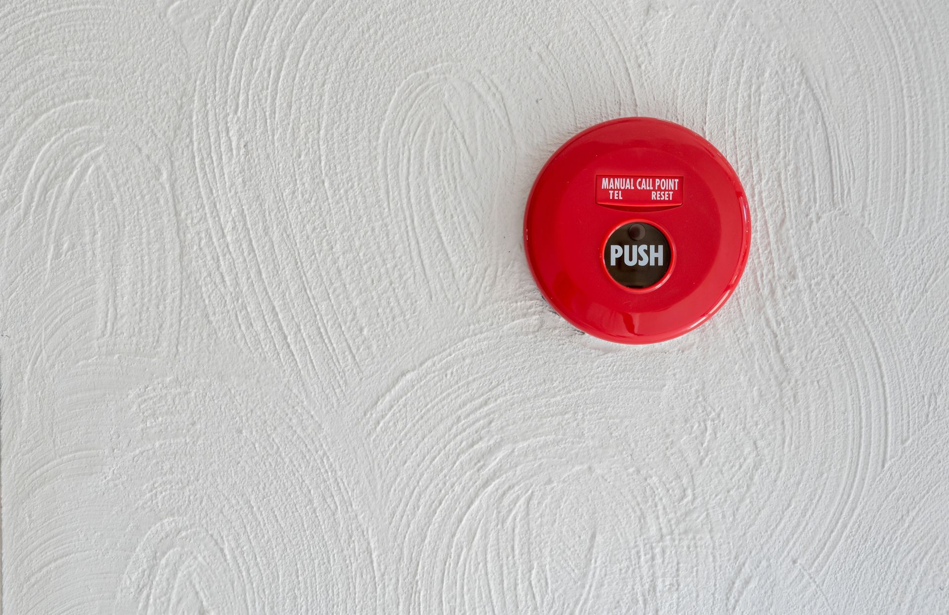 A red manual fire alarm button on a textured white wall. A red manual fire alarm button on a textured white wall.