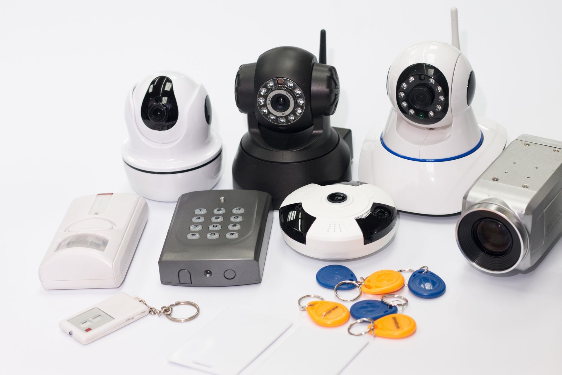 Security cameras, key fobs, and control devices arranged neatly on a white background surface.