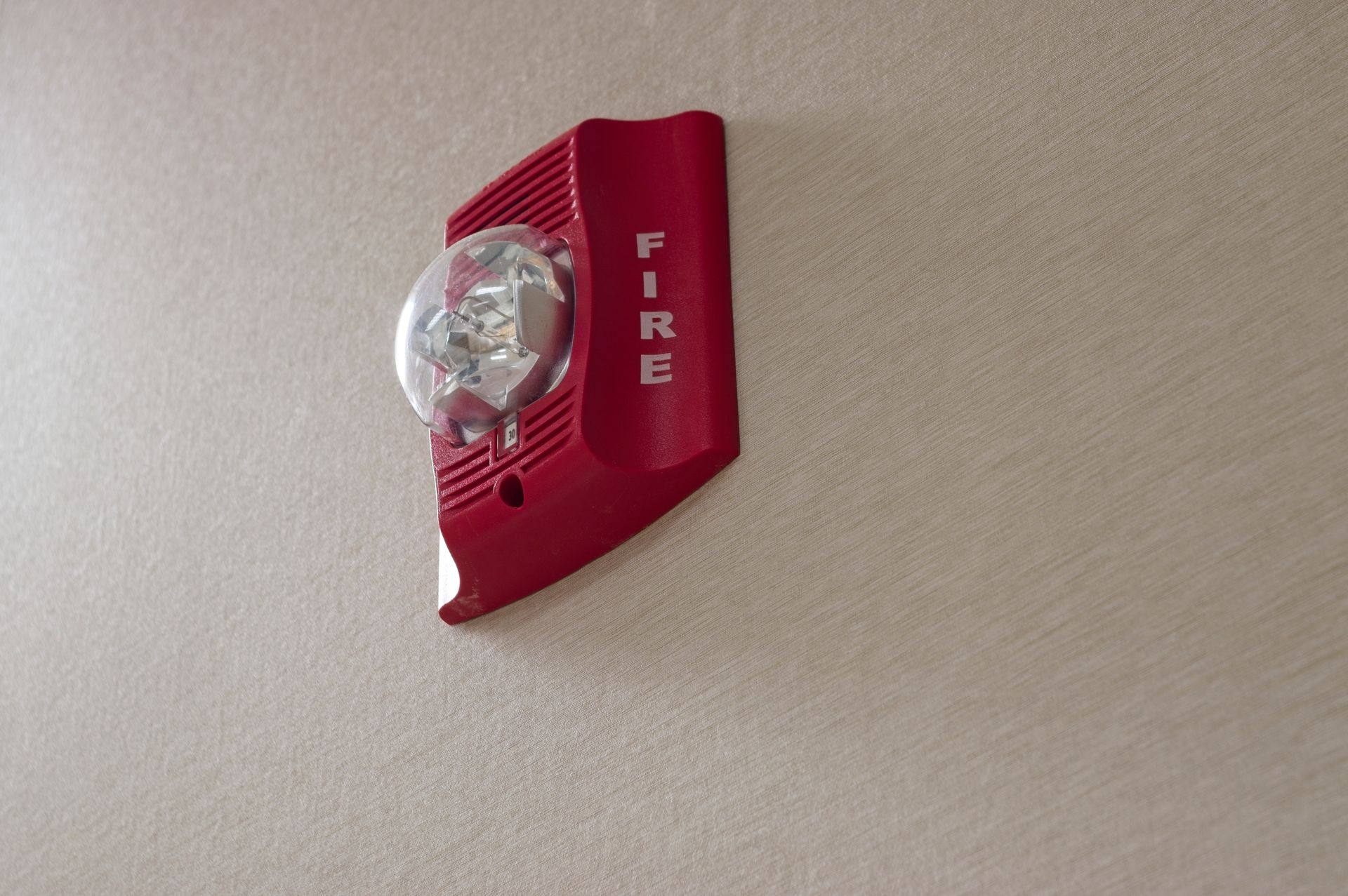 Red fire alarm with strobe light mounted on light-colored wall.