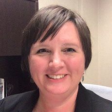 Woman with short brown hair smiles, wearing a black blazer.