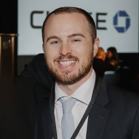 Man smiling, wearing a suit and tie, with a Chase logo in the background.