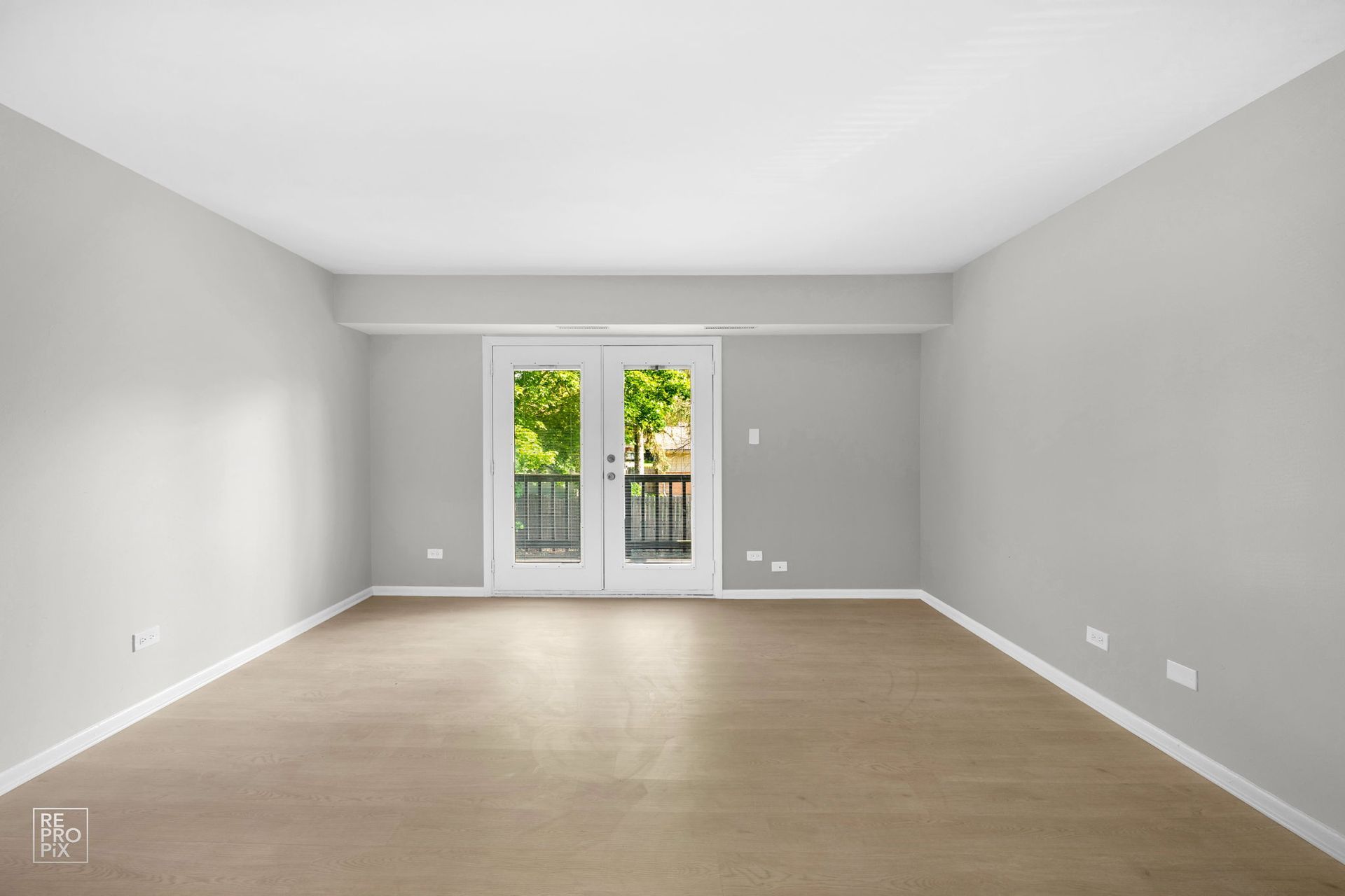 Empty room with light grey walls, beige carpet, and French doors leading to a balcony.