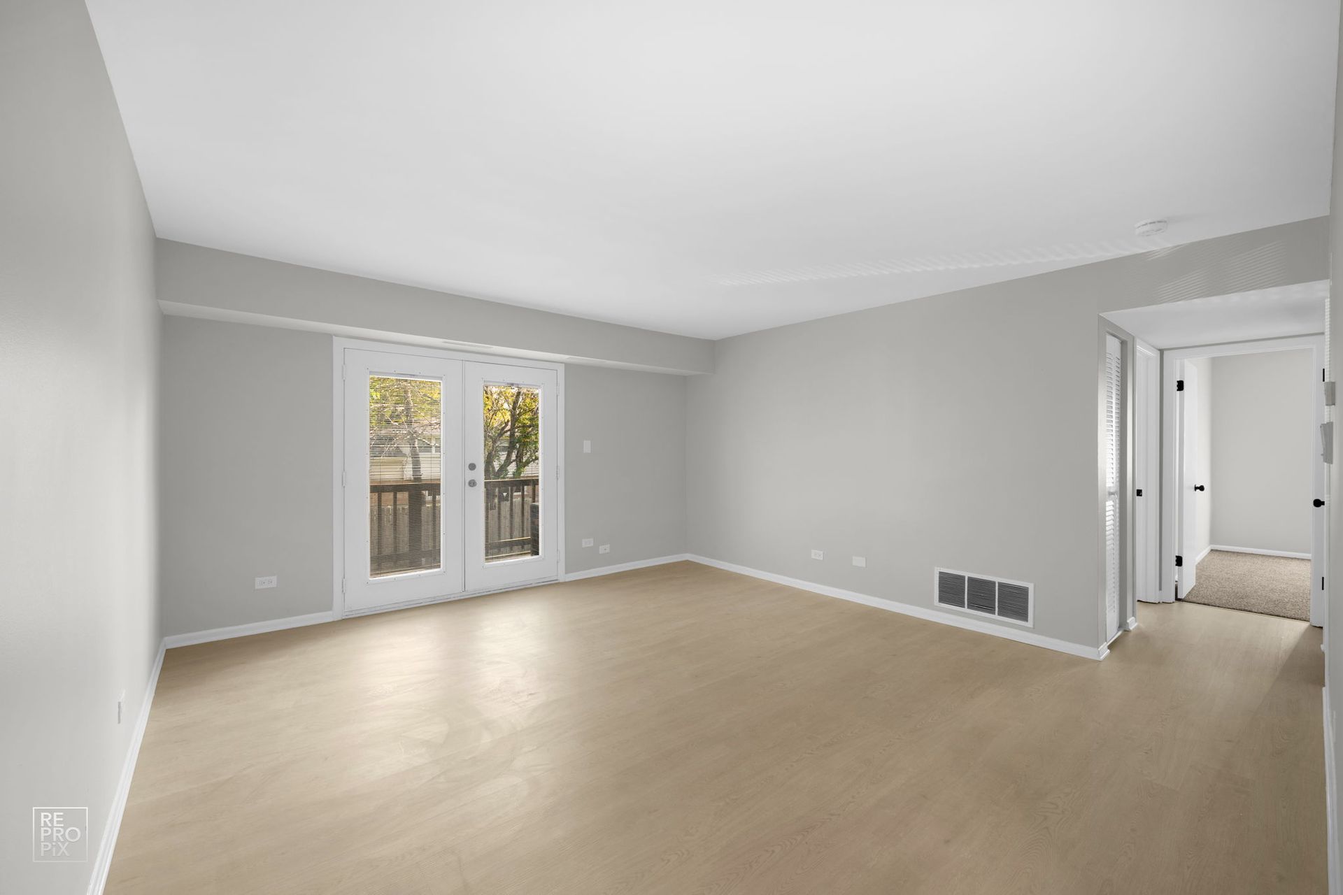 Empty living room with French doors and beige flooring. Gray walls and doorway to hallway.