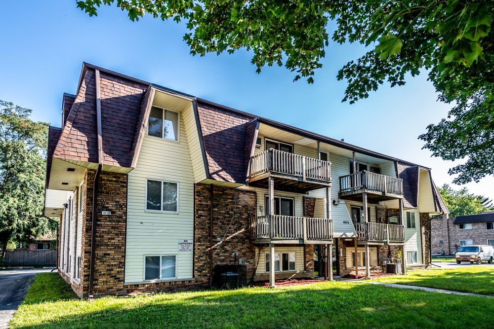 Apartment building with brown roof and balconies, brick and beige siding, on a green lawn.