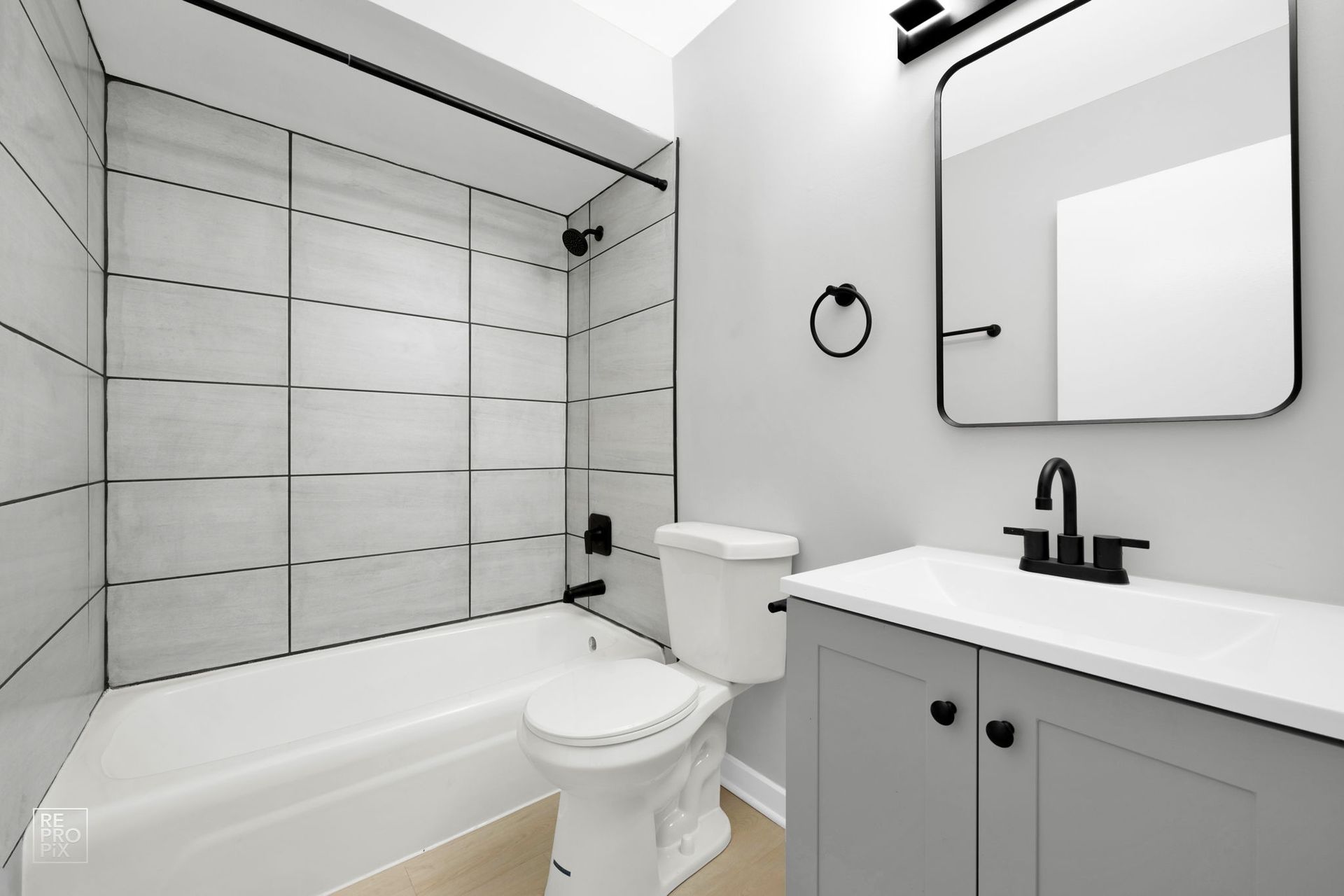 Bathroom with white tile shower, gray vanity, black fixtures, and a toilet.