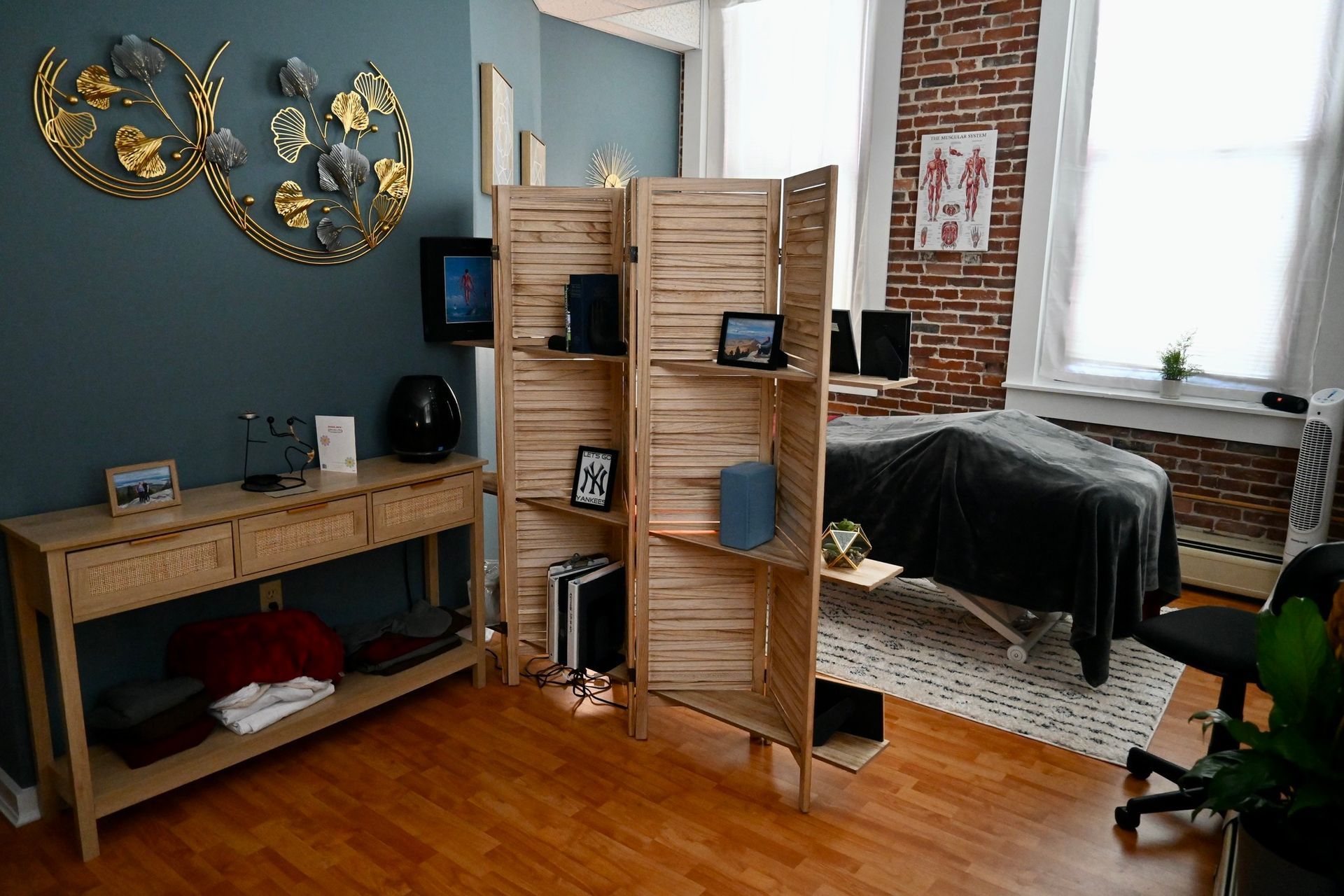 A room with a brick wall , a table , a chair and a bed.