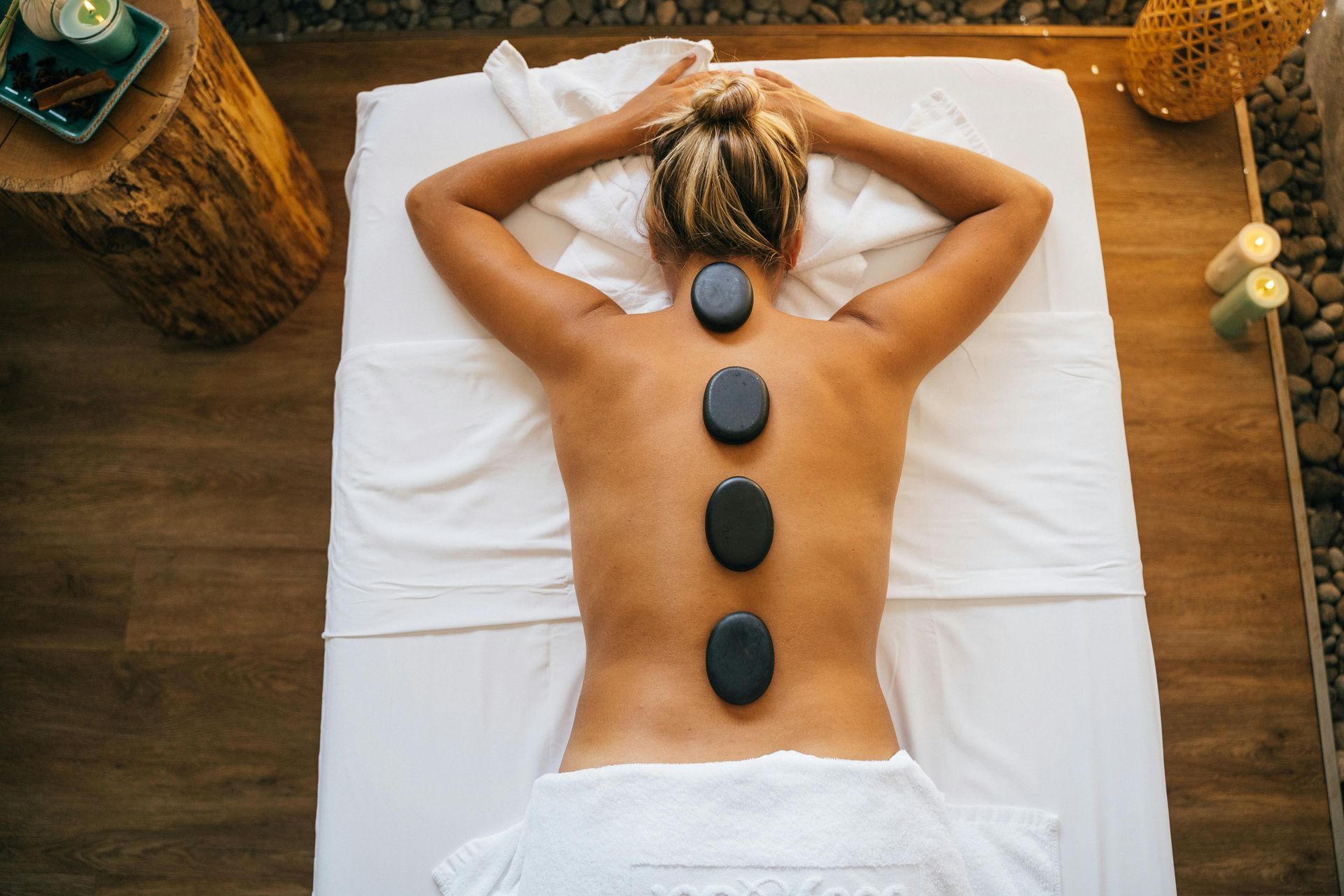 Person lying face down on a massage table with hot stones along the back in a spa setting