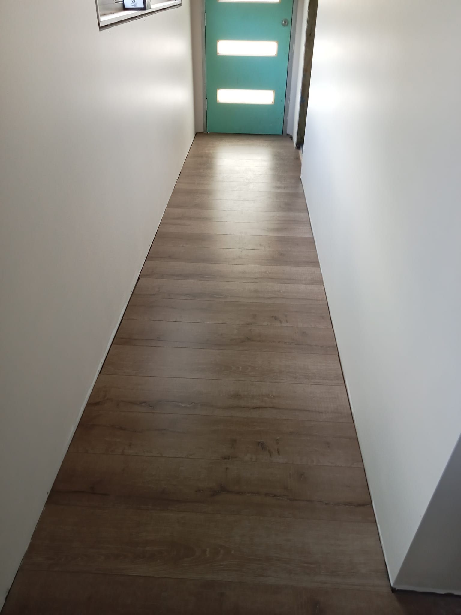 A Hallway With Wood-look Flooring Leads to a Turquoise Door — BLB Flooring Solutions in Maitland, NSW