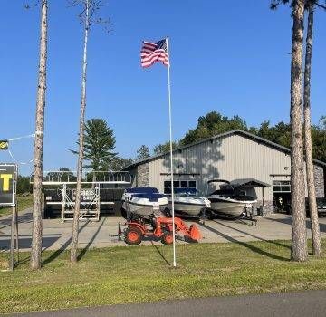 Boats displayed outside a gray building with an American flag. A tractor is in front.