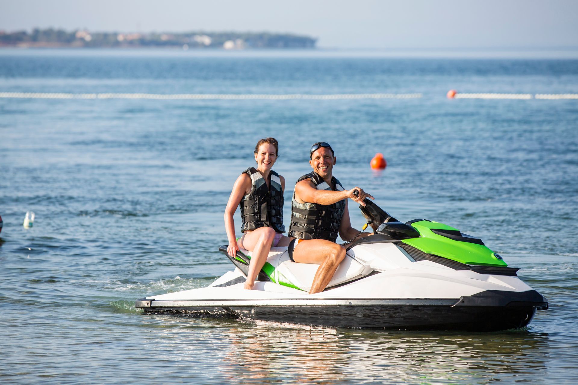 Two people on a jet ski in the ocean, both wearing life vests.